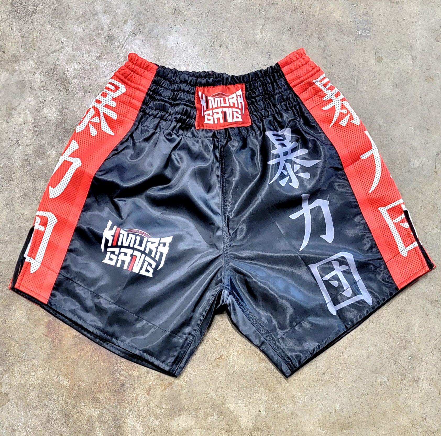 Black shorts with red and white text on a concrete surface